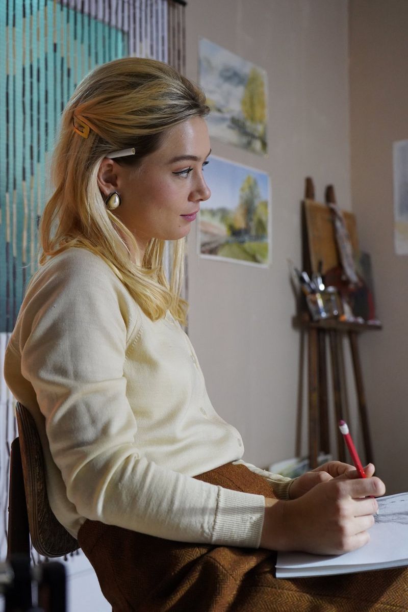A seated blonde woman holding a notebook and pencil. 