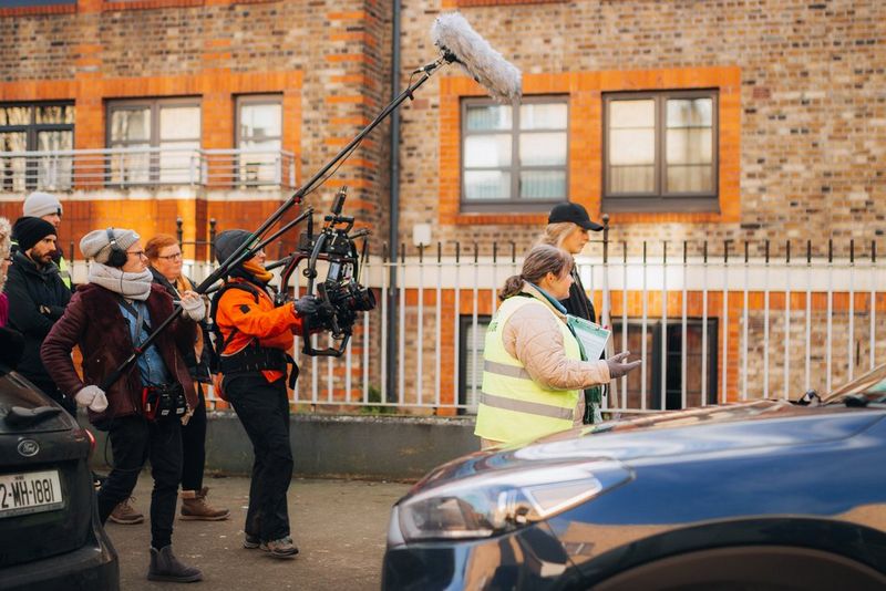 Two female actors walk along a pavement, with a selection of camera crew following and filming them for a scene from the film Verdigris.