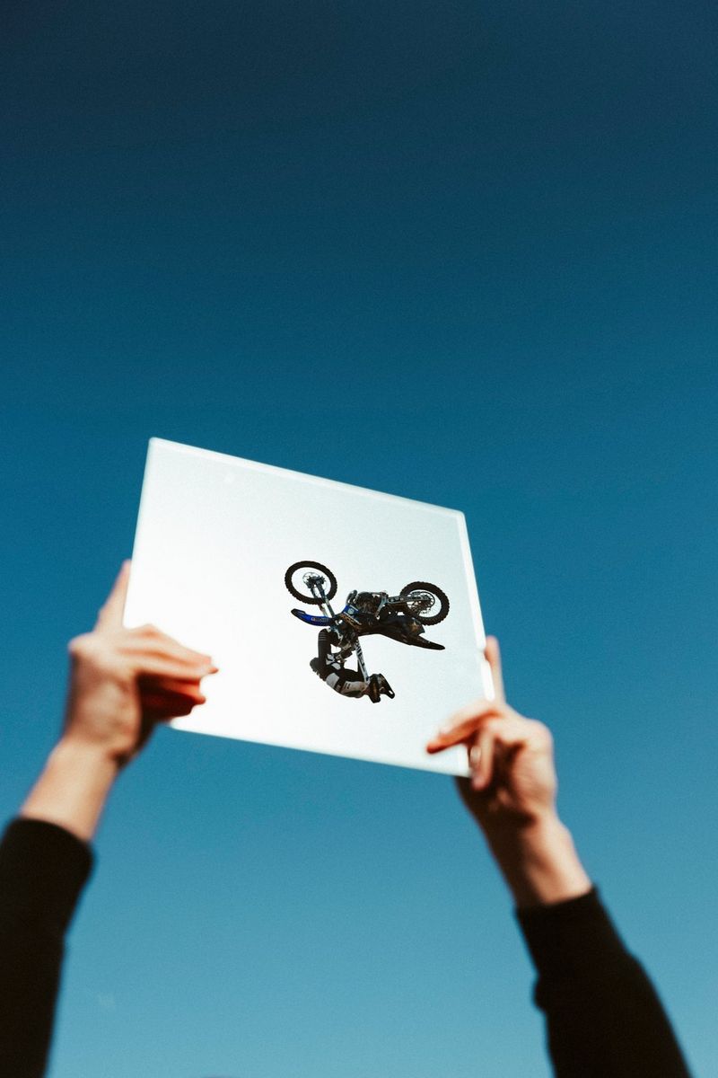 Un uomo che esegue uno stunt in moto riflesso in uno specchio tenuto in alto dalle mani di una persona. Scatto realizzato con Canon EOS R5 da Teddy Morellec.