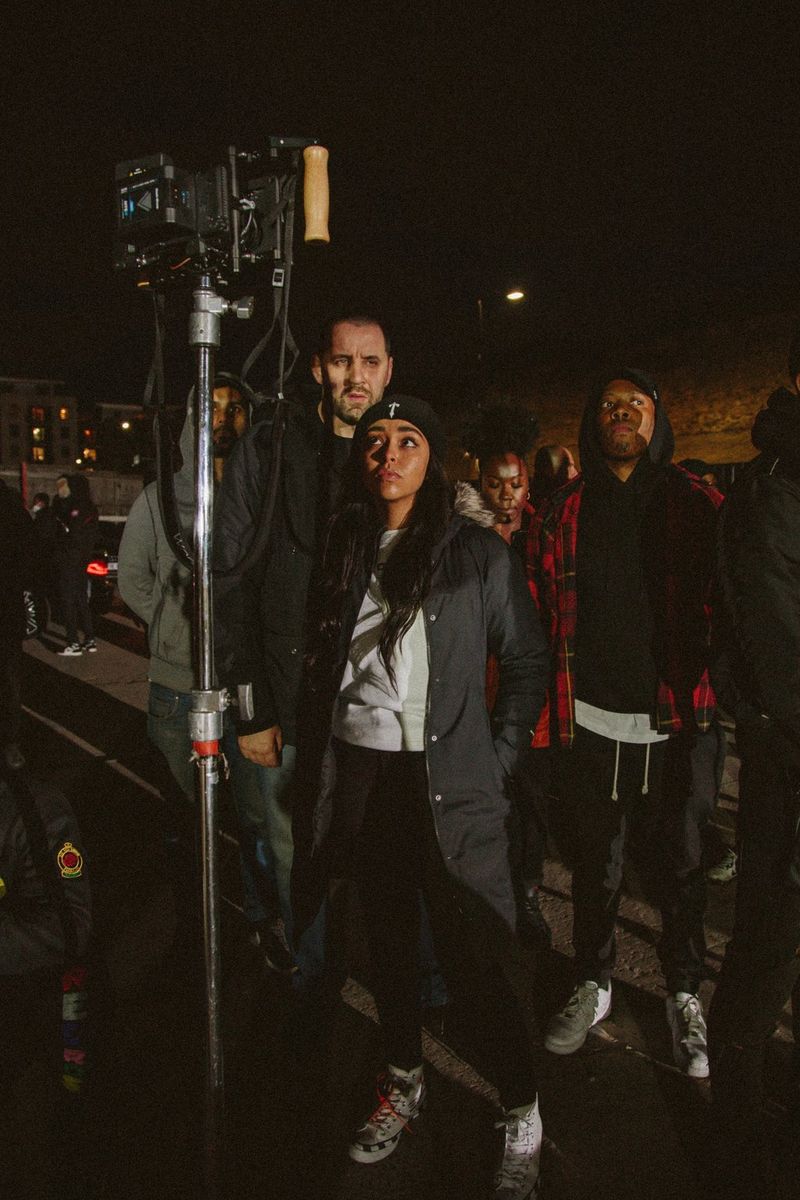 Во время ночных съемок видеограф Эшли Джейди пристально смотрит на экран камеры. Вокруг нее собралась съемочная группа и актеры.