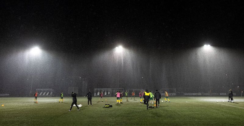 In a photo taken on a Canon EOS R3 by Eddie Keogh, football players practise under the floodlights on a dark and rainy night.