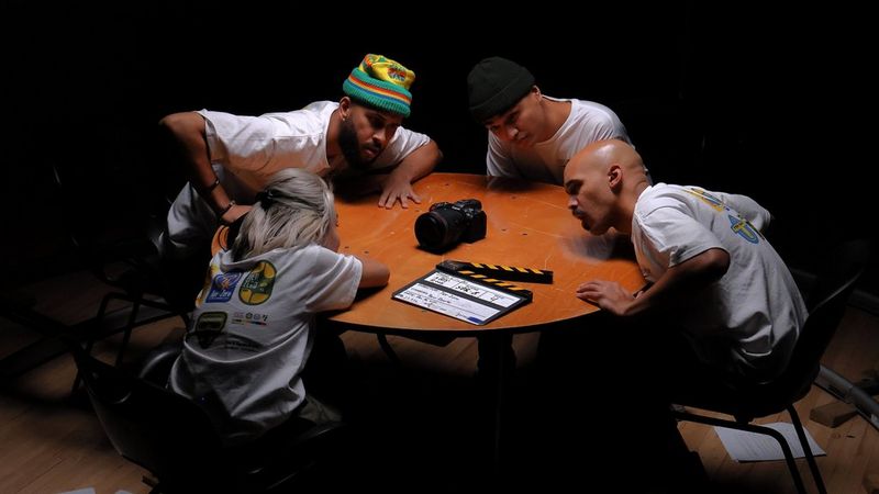 Vier mensen zitten aan een ronde tafel en leunen naar voren om te kijken naar de Canon EOS R5 C in het midden van de tafel.