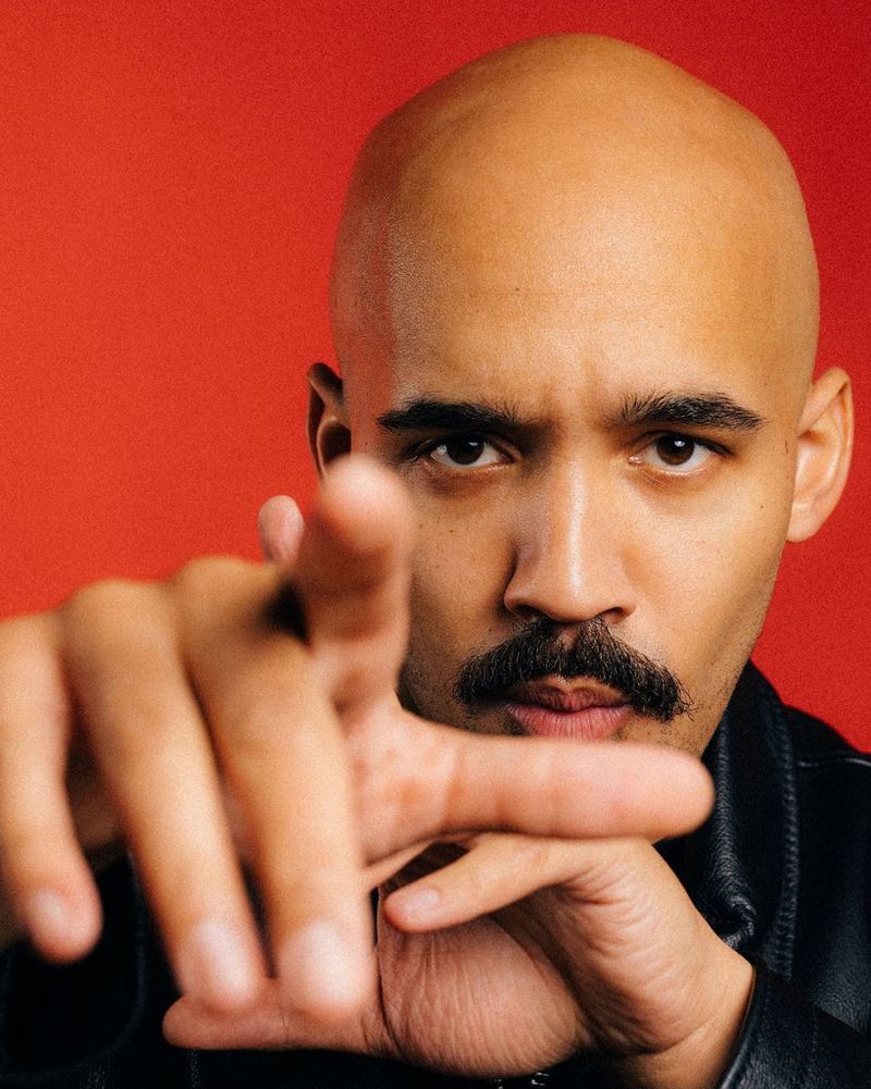 Een portretfoto van Charlie Lindsay tegen een rode achtergrond.