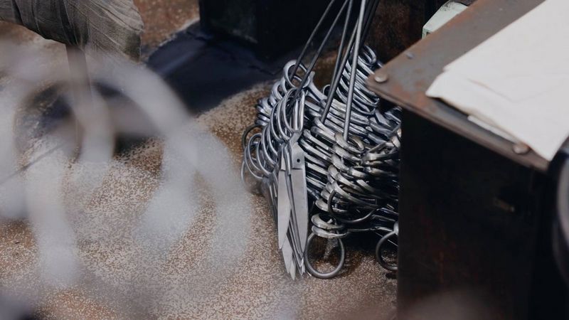 Handcrafted scissors piled on metal supports next to a wooden table, in a still from a video shot on a Canon EOS R5 C by Tom Barnes. 