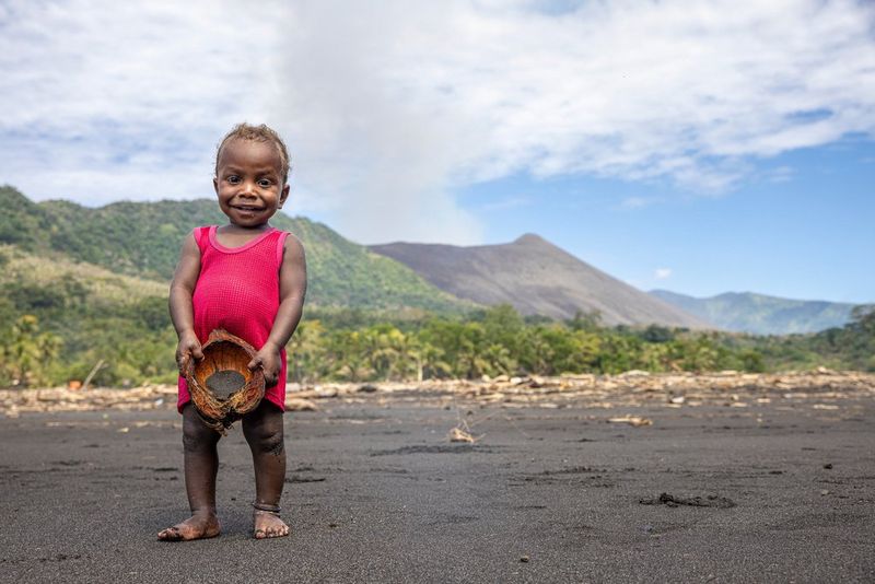 Фотография Уллы Лохманн, снятая на камеру Canon EOS R5, изображает ребенка в ярко-красном платье на фоне дымящегося вулкана