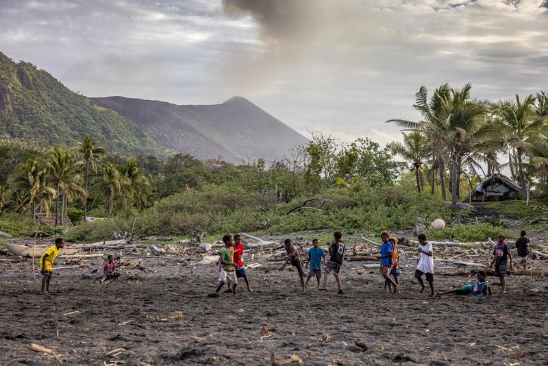 На фотографии Уллы Лохманн, снятой с помощью камеры Canon EOS R5, изображена группа детей, играющих в футбол на фоне местной растительности и дымящегося вулкана.