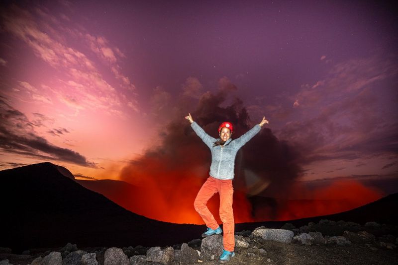 На фотографии, снятой на камеру Canon EOS R5 сыном Мануком, Улла, подняв руки вверх, стоит перед извергающим лаву и дым вулканом.