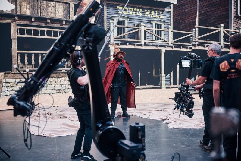 Een virtuele productieset-up met Canon-camera's op een gimbal en op een kraanarm die een acteur met een cape aan en een spitse hoed op filmen vóór een projectie van een straatscène in het Wilde Westen.