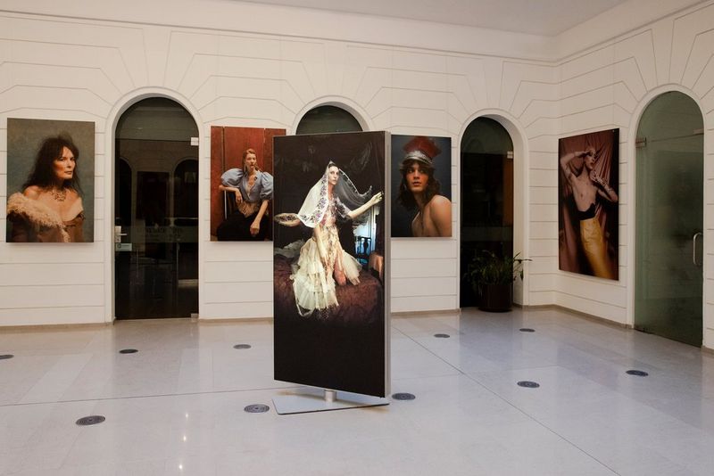 Four portraits mounted on a gallery wall behind a large image on a freestanding board. 