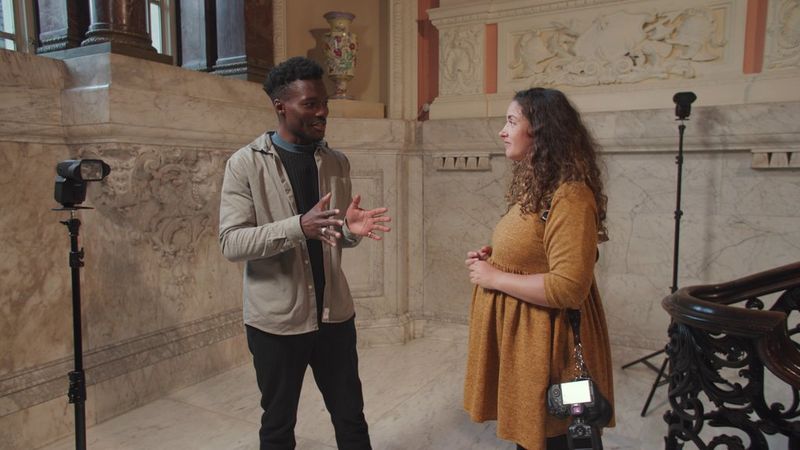 Il content creator in tema di tecnologia Tomi Adebayo e la fotografa Alison Bounce si trovano sul pianerottolo di una scala. Alison ha una fotocamera Canon EOS R5 appesa a una spalla e sono visibili due Speedlite Canon su supporti di fianco a loro.