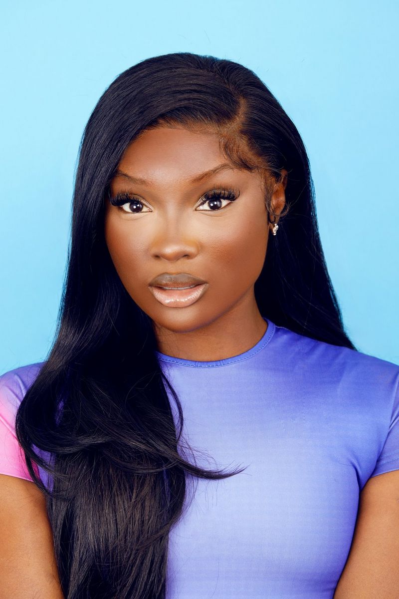 A portrait photo taken by Jade Keshia Gordon of a woman with long dark hair in a purple top against a blue background looking at the camera.