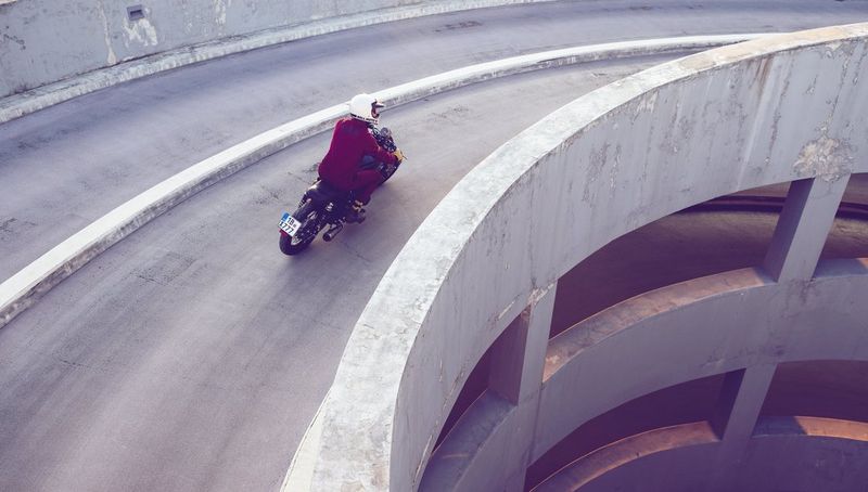 A person on a motorbike rides down a curved concrete road. 