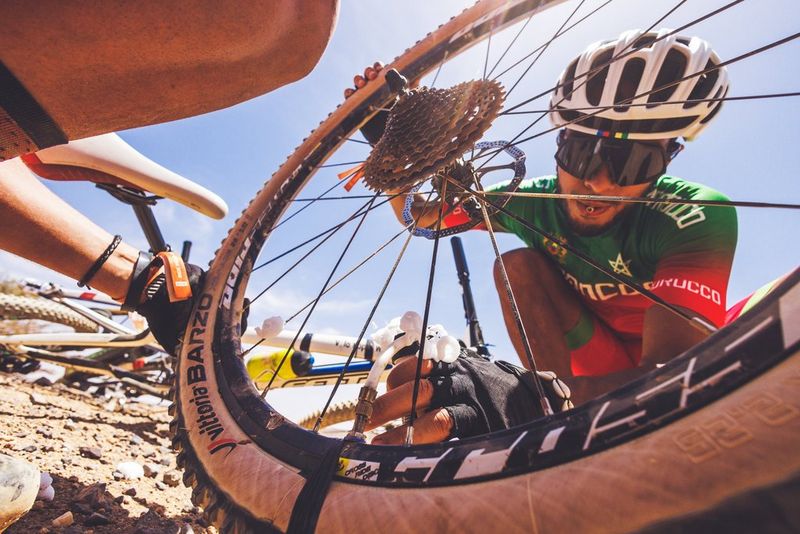 A close-up of cyclist attending to a bike wheel on a sunny day. 