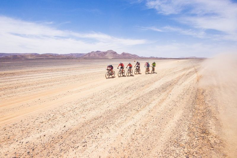 Six cyclists ride in the centre of the shot surrounded by desert landscape.