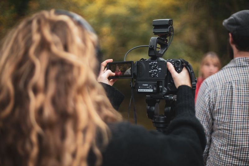 Photo prise par-dessus l'épaule d'une femme qui filme un couple qui parle avec un appareil Canon.