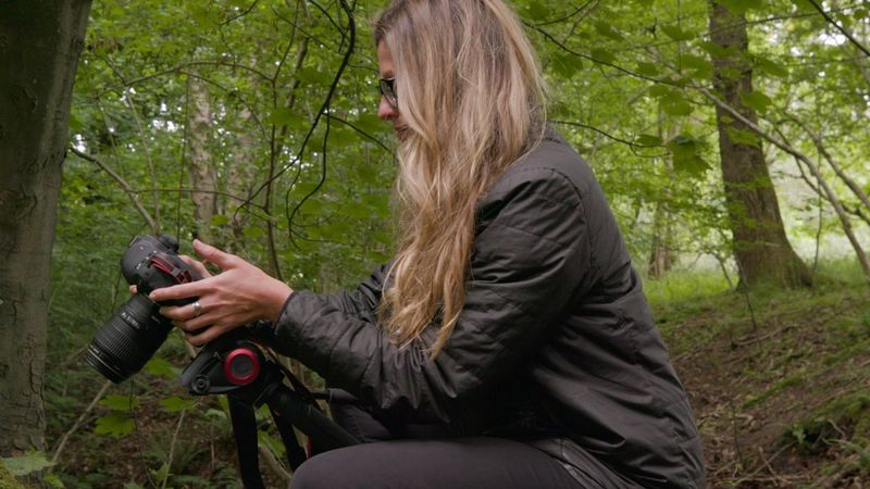 Une femme dans les bois s'est accroupie pour régler son appareil Canon.