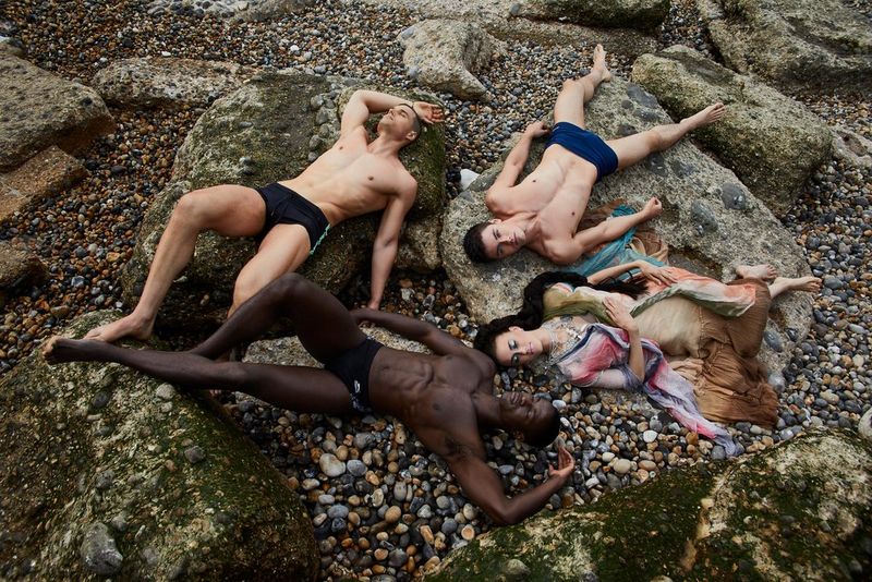 Drie mannen in korte broek en een vrouw in een jurk liggen op keien en kiezels, vastgelegd met een Canon EOS 5D Mark IV.