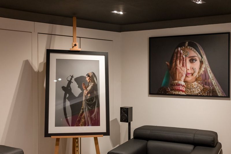 Een kleine, witte showroom met een comfortabele zwarte leunstoel in het midden, een grote fotoprint op de muur erachter en een ingelijste fotoprint op een ezel ernaast.