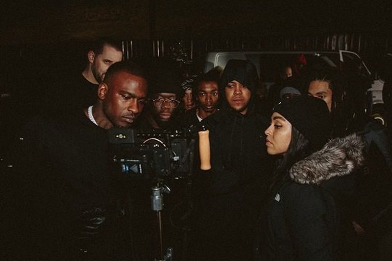Director Ashleigh Jadee stands behind her camera, while a group of men watch her work.