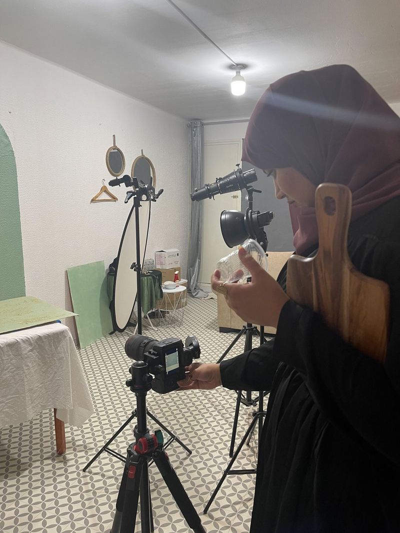 Food photographer Yasmin Albatoul gazes into her Canon camera on top of a tripod while holding a plastic cup and clutching a wooden chopping board. Shot on Canon.