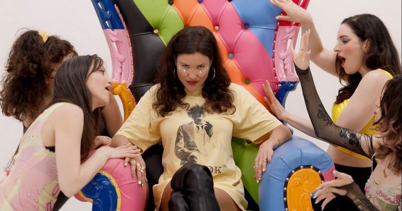 Filmmaker and actor Brianna Lee sits on a coloured chair in her film The Troll, surrounded by other woman.