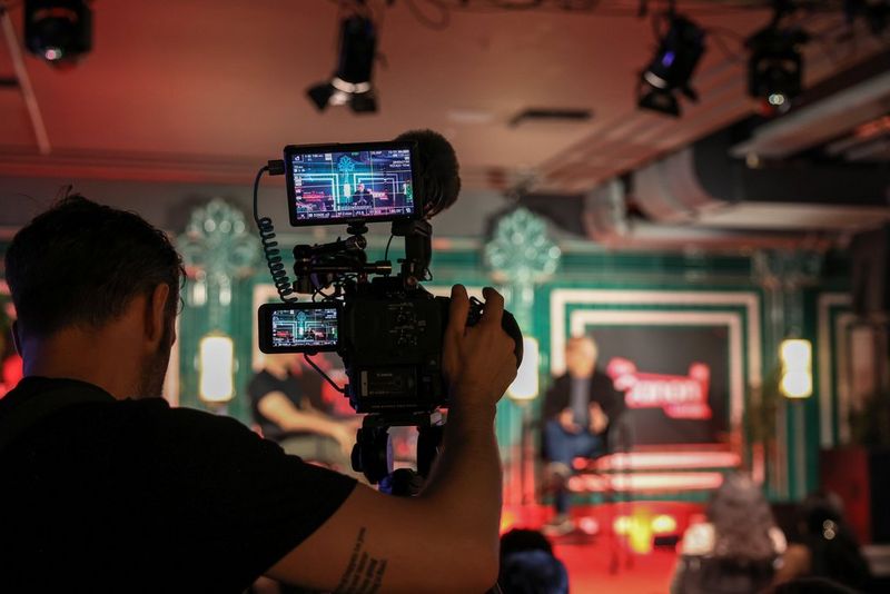 An over the shoulder shot of the back of an EOS C80 camera, showing Haris Zambarloukos sitting on a stage on the LCD screen and monitor at the Raindance Film Festival 2026. 