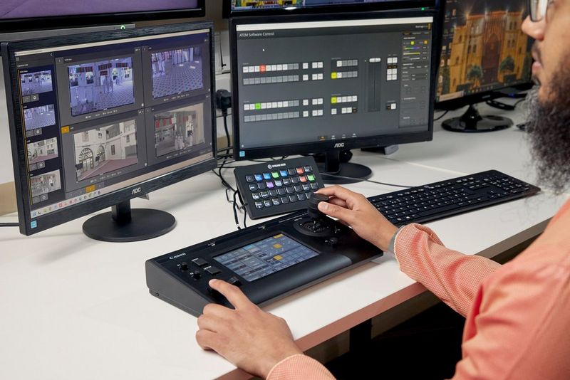 Un uomo al lavoro su un controller PTZ Canon RC-IP100 collegato a due schermi digitali.