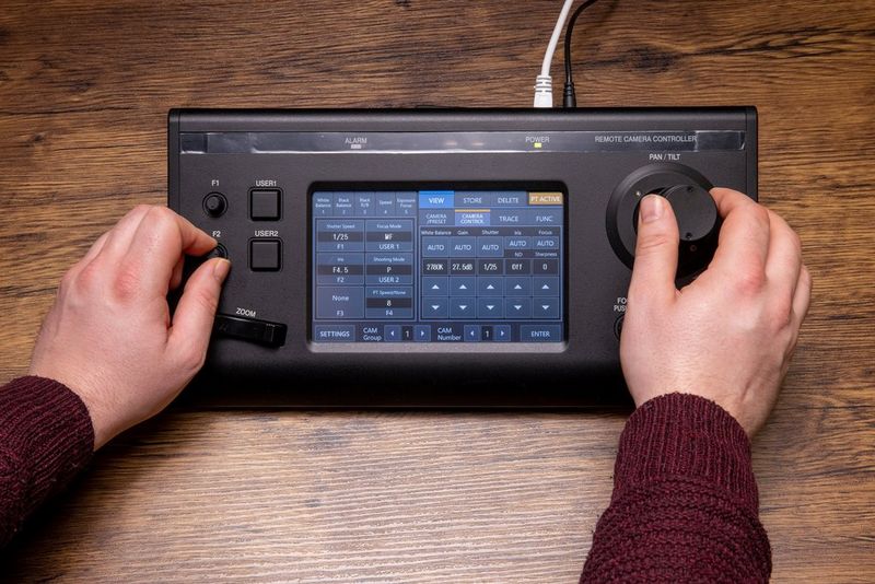 De camera-afstandsbediening Canon RC-IP100 ligt op een houten oppervlak en wordt door handen bediend.