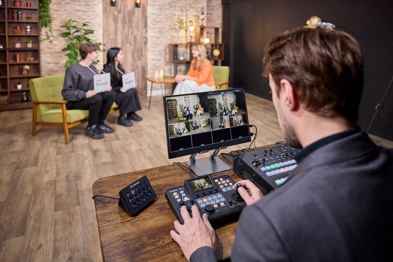 A user with a Canon RC-IP300 remote camera controller and a screen monitoring multiple camera feeds.