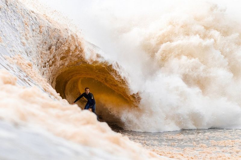 In a photo taken by Luca Salisbury, a surfer in a wetsuit rides the tube as a muddy brown coloured wave breaks over him, creating a huge plume of spray.