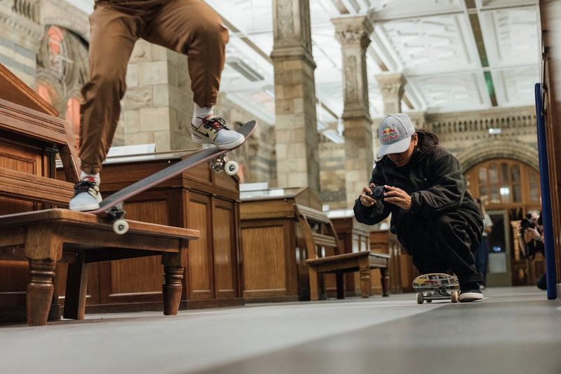 Una persona è accovacciata su uno skateboard, con in mano Canon PowerShot V10, e filma un'altra skater mentre esegue un salto.