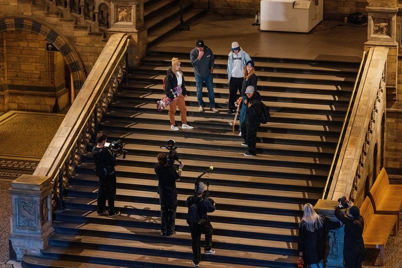 Le skater e la troupe in piedi su una scalinata in una delle sale del Natural History Museum di Londra.
