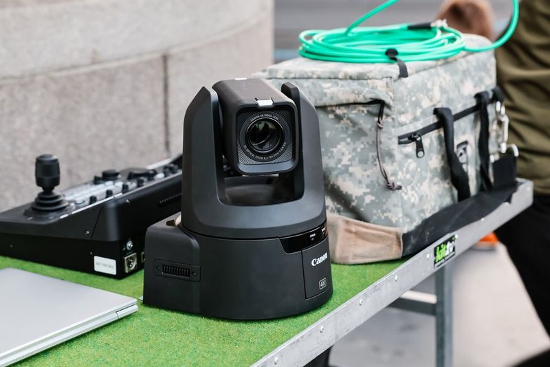 A Canon PTZ camera on a tabletop with an RC-IP1000 controller and a large kitbag on the table behind it, part of the kit used to film the Red Bull wingsuit flight.