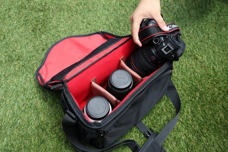 A hand lifts out a camera from a kitbag, which also includes two other lenses.