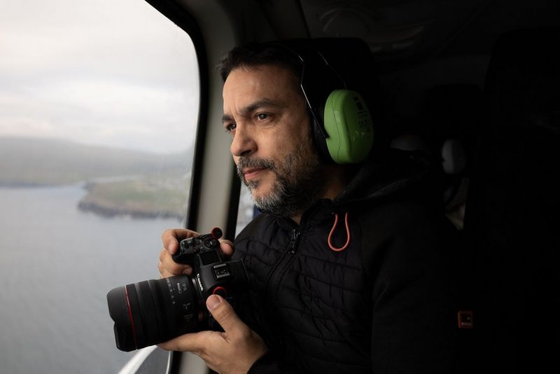 Joel Santos holds a Canon camera with a Canon RF 10-20mm F4L IS STM lens while looking out the window of a helicopter. 