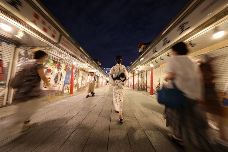 O stradă aglomerată în Japonia, cu oameni care se îndepărtează de aparatul foto, estompaţi.