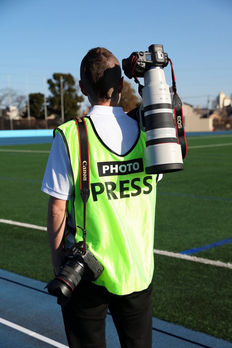 Een fotograaf met een reflecterend hesje draagt een camera met daarop de RF 100-300MM F2.8L IS USM hangend over een schouder.