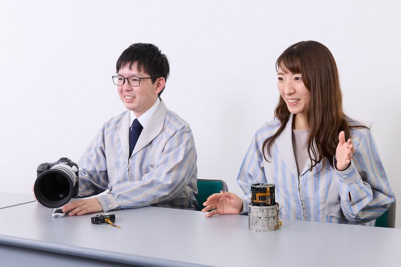 Twee van de ontwikkelaars van de RF 100-300MM F2.8L IS USM zitten aan een tafel, een met het objectief voor zich en de ander met een deel van het mechanisme.