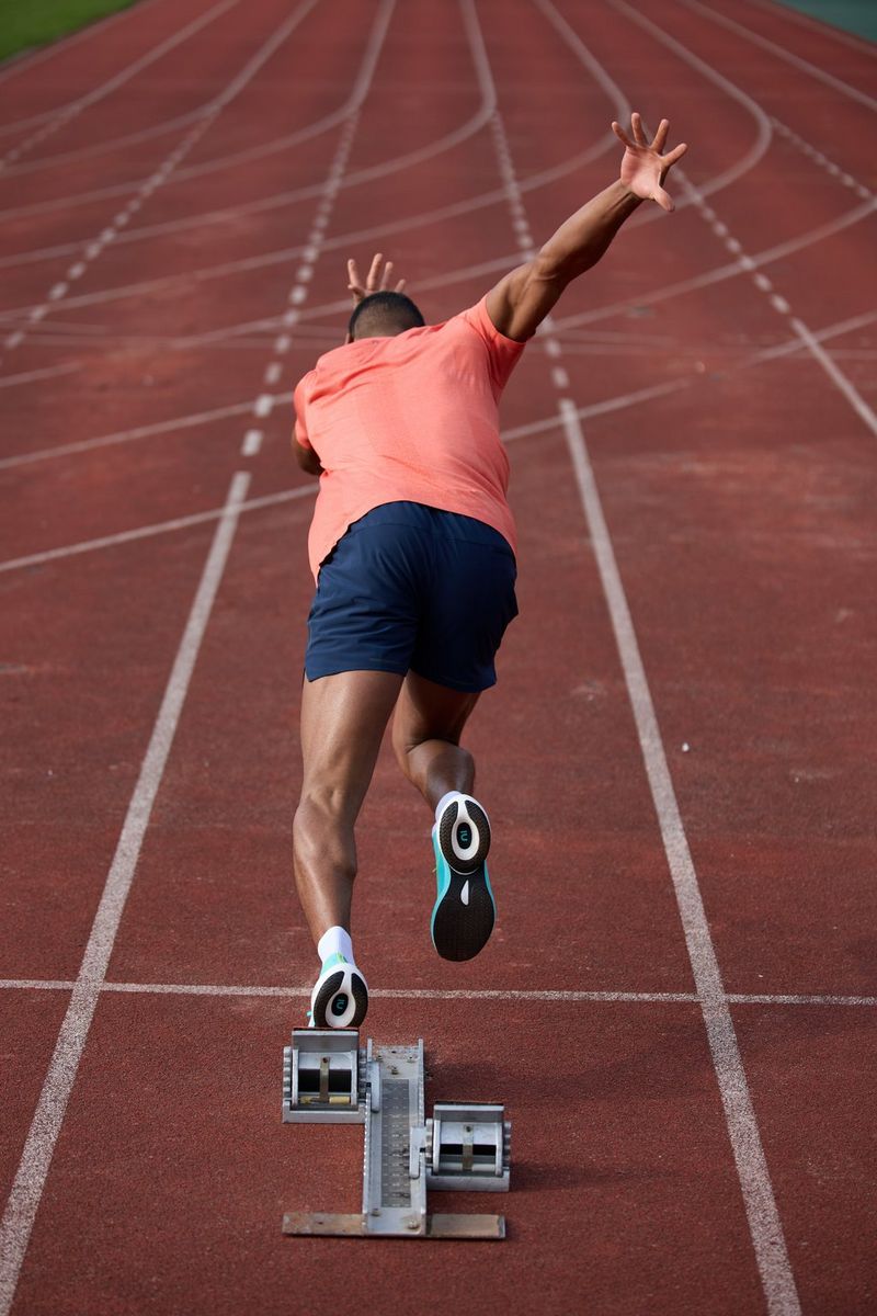An athlete is captured from behind sprinting from the starting line, their hands outstretched, in a photo by Julian Finney taken on a Canon RF 100-300mm F2.8L IS USM lens.