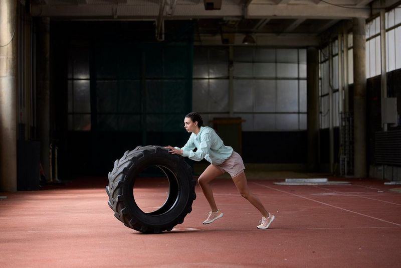 An athlete pushes a large tyre across a sports hall, in a photo taken with a Canon RF 100-300mm F2.8L IS USM lens.