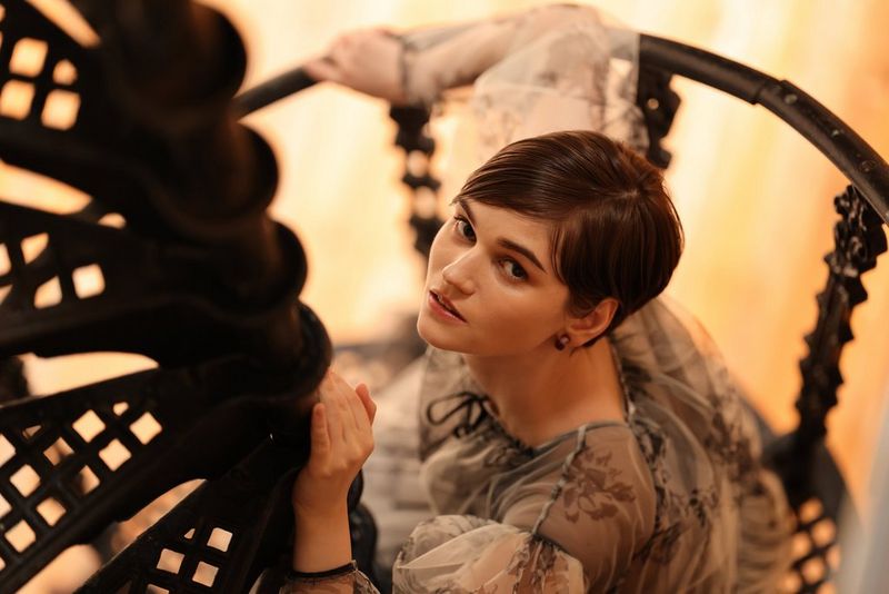 אישה יורדת במדרגות לולייניות ומביטה למצלמה.