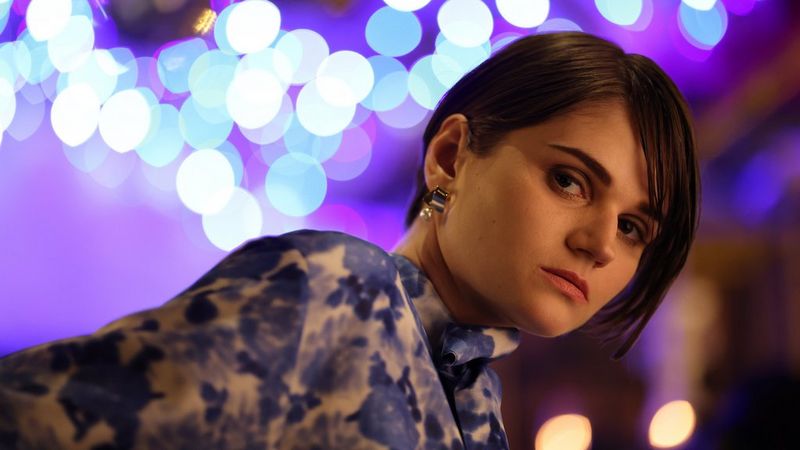 A low-lit portrait of a woman against a background of distinctive white and pale blue circular bokeh.
