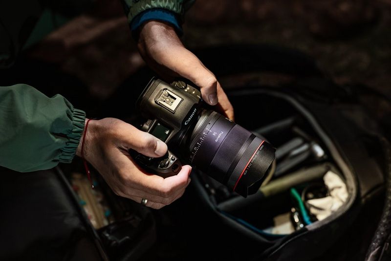 Een RF 14mm F1.4L VCM-objectief op een Canon EOS-systeemcamera die boven een cameratas wordt gehouden. De tas wordt in een donkere omgeving verlicht door de hoofdlamp van de fotograaf.