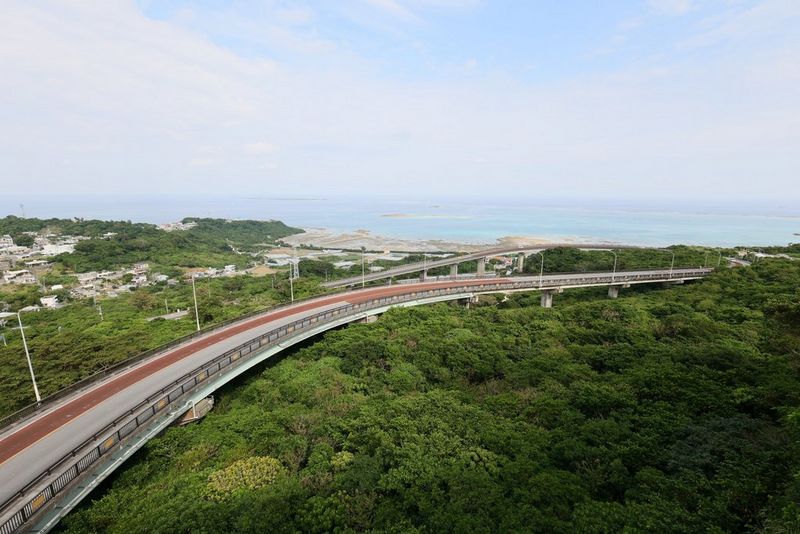 Истата сцена, со поглед кон море над бујно зеленило и подигнат пат што го сече, но со забележливо поширока перспектива. Снимено со широкоаголен објектив Canon RF 15–30mm F4.5-6.3 IS STM.