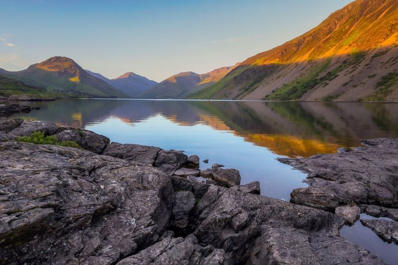 Un lago circondato da montagne, la cui cima è illuminata dalla luce dorata del sole.