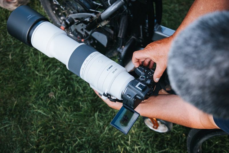 A Canon camera with a Canon RF 200-800mm F6.3-9 IS USM lens attached being held low to the ground by a person in a wheelchair. 