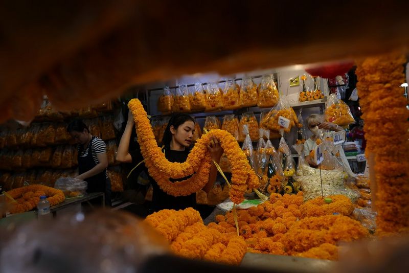 A young woman carries a garland of bright orange flowers in a shop. Travel photo taken with a Canon RF 20mm F1.4L VCM lens.