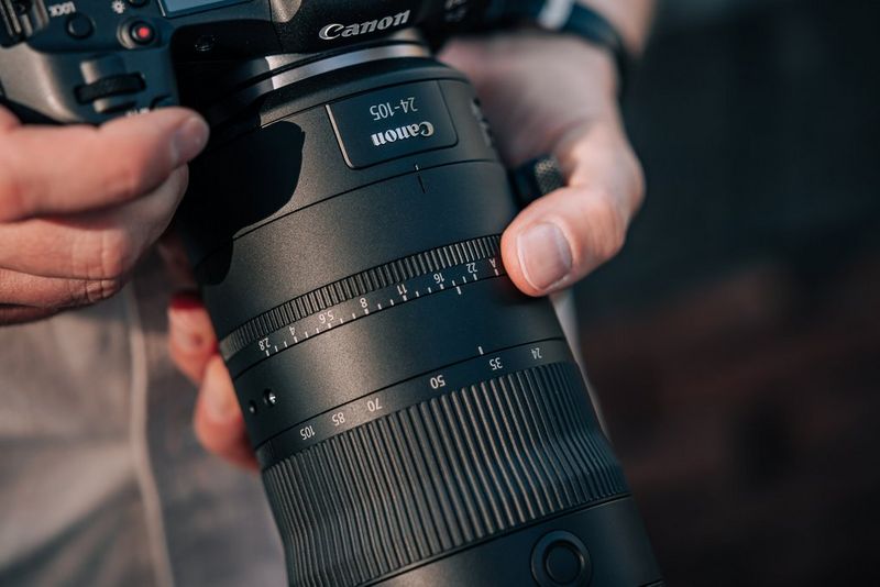 A close-up of a pair of hands holding the iris ring on the Canon RF 24-105mm F2.8L IS USM Z lens.
