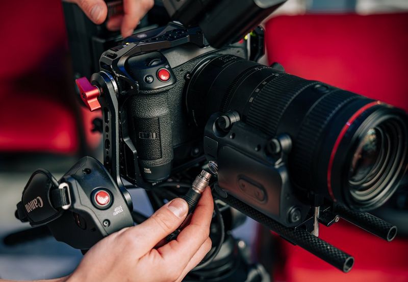 Een gebruiker staat op het punt om de kabel van een Power Zoom-adapter PZ-E2B te verbinden met de 20-pins aansluiting op een Canon RF 24-105mm F2.8L IS USM Z-objectief.
