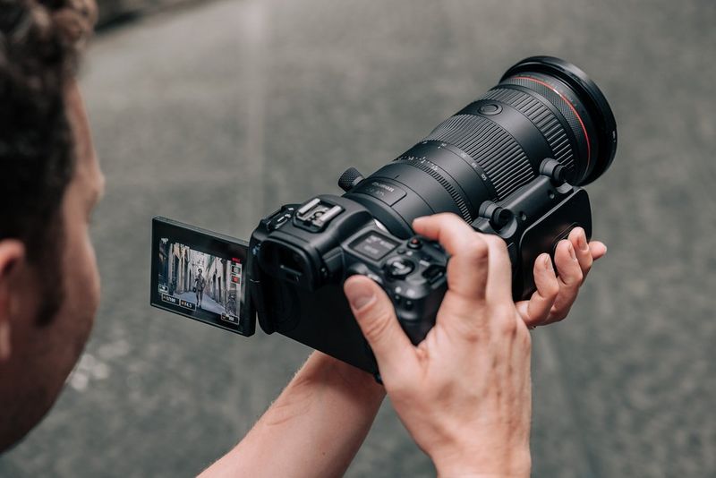 Hands holding a Canon camera with a Canon RF 24-105mm F2.8L IS USM Z lens and Canon Power Zoom Adapter PZ-E2B attached.